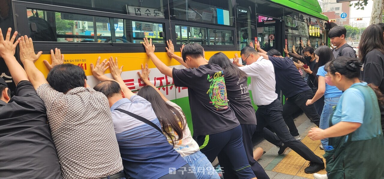버스에서 하차후 넘어져 바퀴에 낀 할머니를 구하기 위해 오류동역버스정류장에 있던 주민들이 일제히 버스를 들어올리기위해 힘을 쓰고 있다.